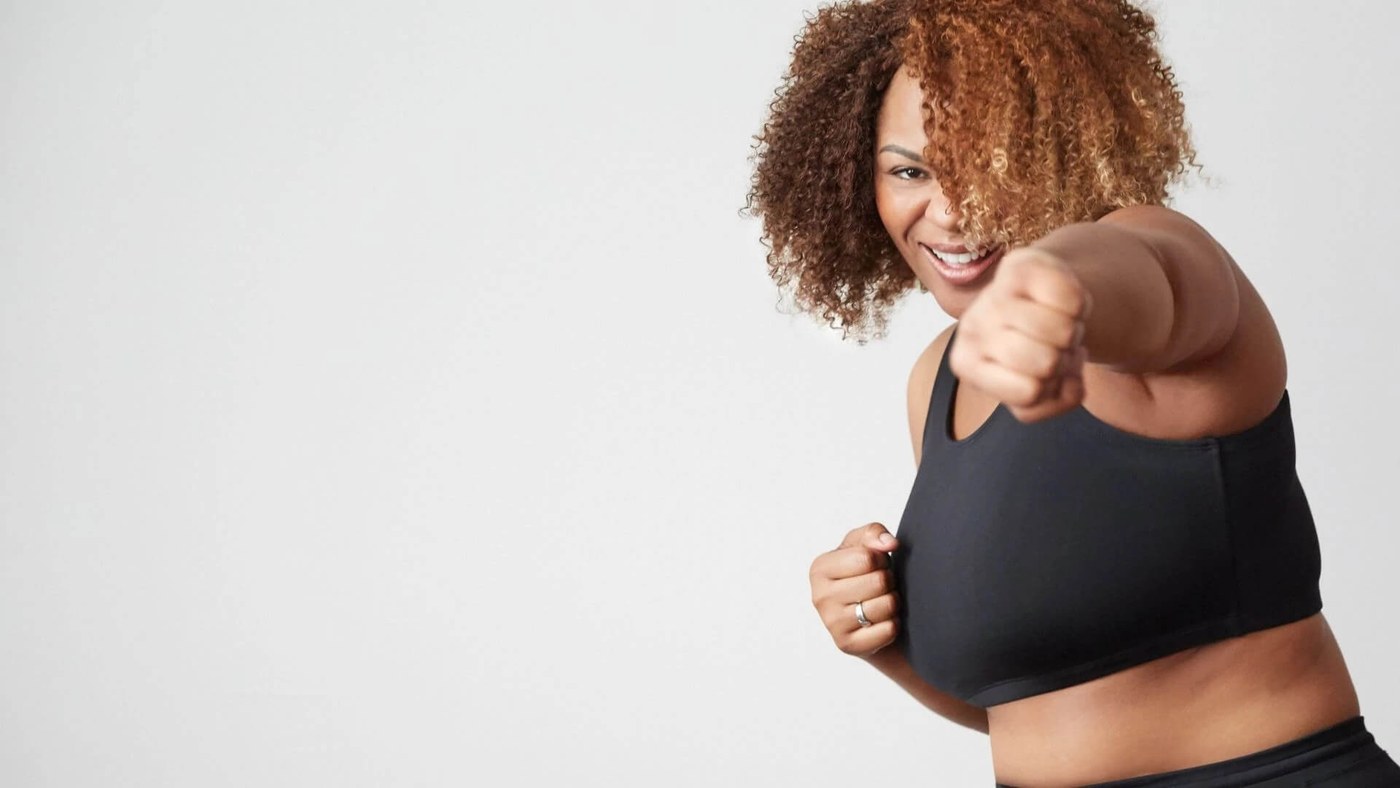 Plus size woman smiling, facing front while punching towards camera wearing JunoActive plus size sports bra.